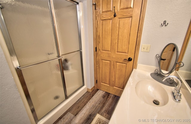 full bath featuring a shower stall, wood finished floors, vanity, and a textured wall