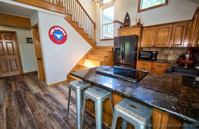kitchen featuring backsplash, a peninsula, black fridge, dark wood-style floors, and stovetop