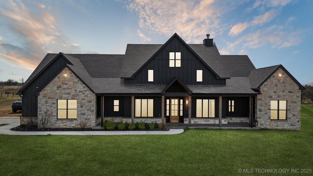 modern farmhouse with a lawn, stone siding, board and batten siding, and roof with shingles