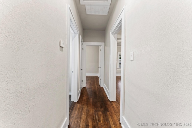 hallway featuring baseboards, wood finished floors, and a textured wall