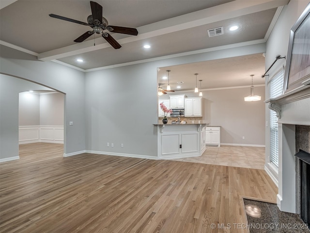 unfurnished living room with visible vents, ceiling fan, a fireplace, ornamental molding, and light wood-type flooring