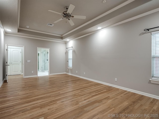 empty room featuring a tray ceiling, crown molding, a ceiling fan, and light wood finished floors