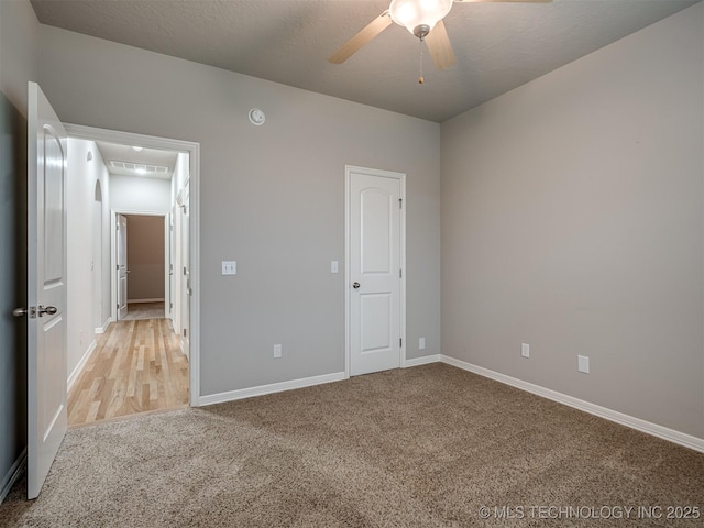 unfurnished bedroom with a textured ceiling, baseboards, ceiling fan, attic access, and light carpet
