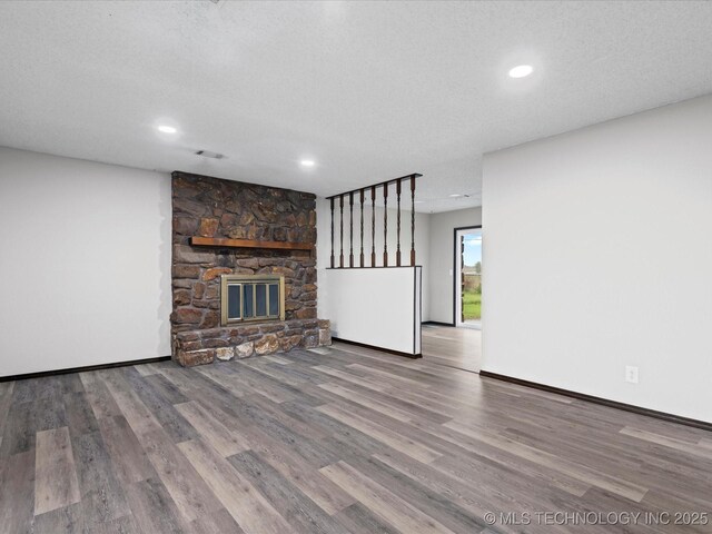 208 NE Spruce Ave, Bartlesville, OK 74006 - unfurnished living room with recessed lighting, baseboards, a textured ceiling, a stone fireplace, and wood finished floors
