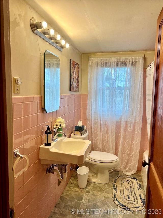 full bath with tile walls, toilet, a sink, shower / bath combo, and wainscoting