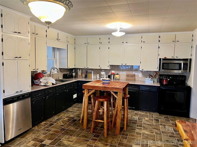 kitchen featuring white cabinets, light countertops, appliances with stainless steel finishes, a sink, and dark cabinets
