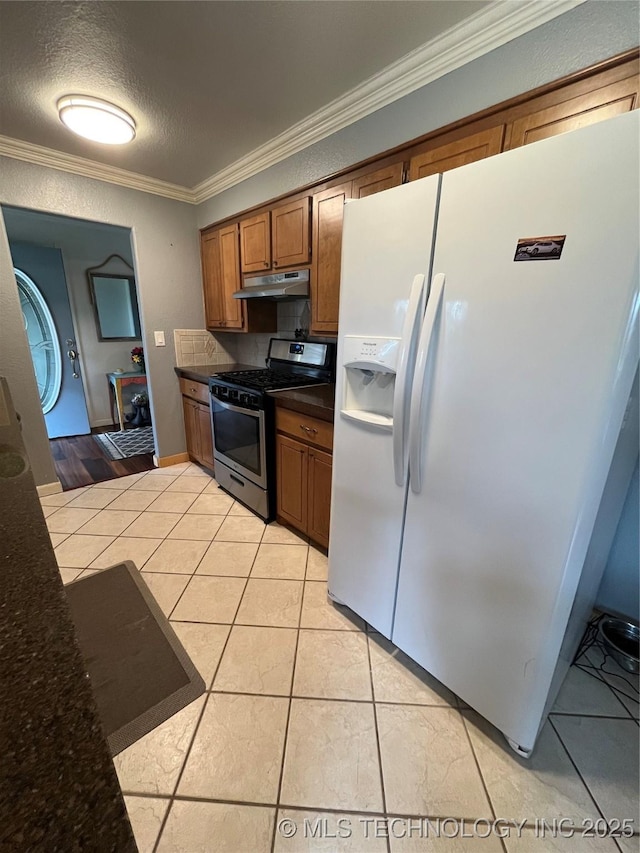 kitchen with crown molding, brown cabinets, white fridge with ice dispenser, stainless steel gas stove, and under cabinet range hood