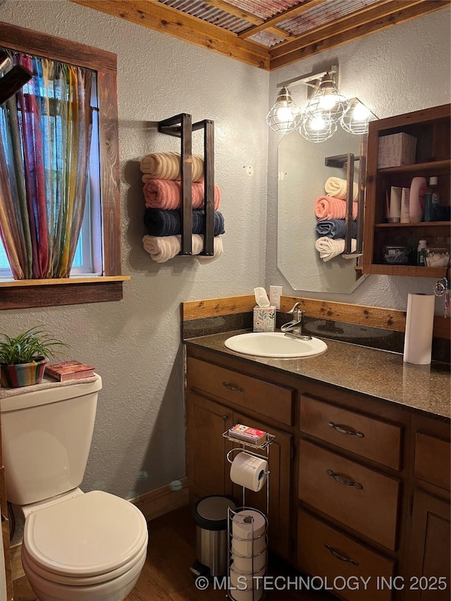 bathroom featuring toilet, baseboards, wood finished floors, a textured wall, and vanity