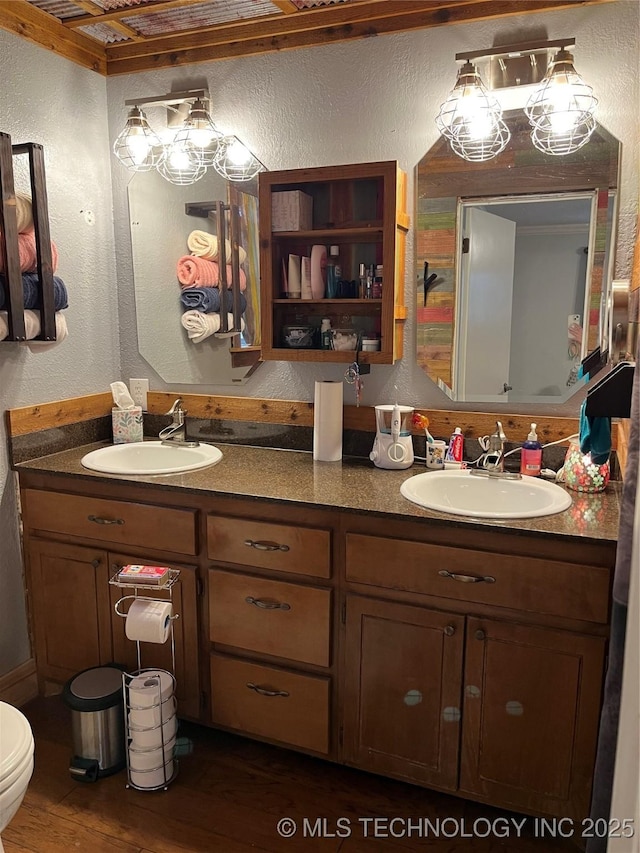 full bath featuring a textured wall, wood finished floors, a sink, and double vanity