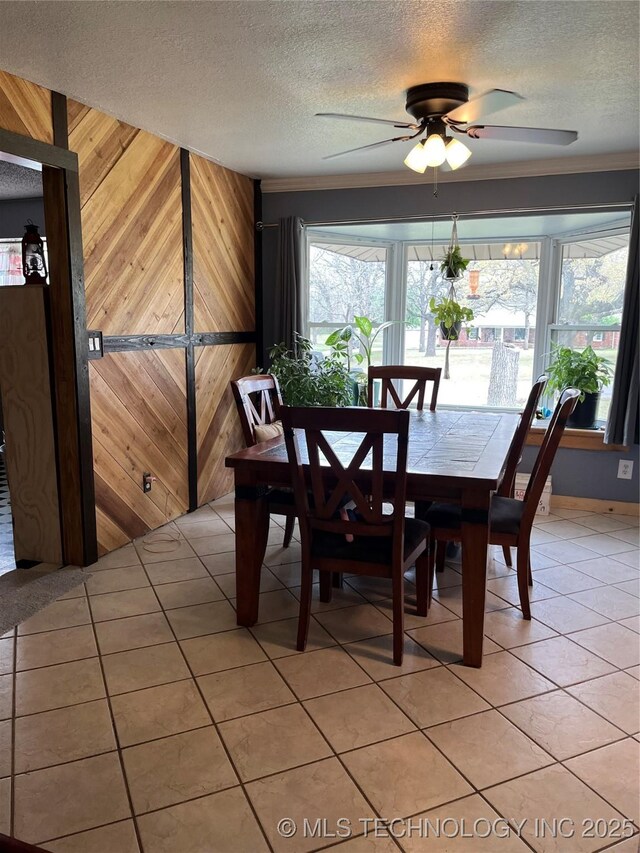 dining space featuring a ceiling fan, crown molding, a textured ceiling, light tile patterned flooring, and wood walls