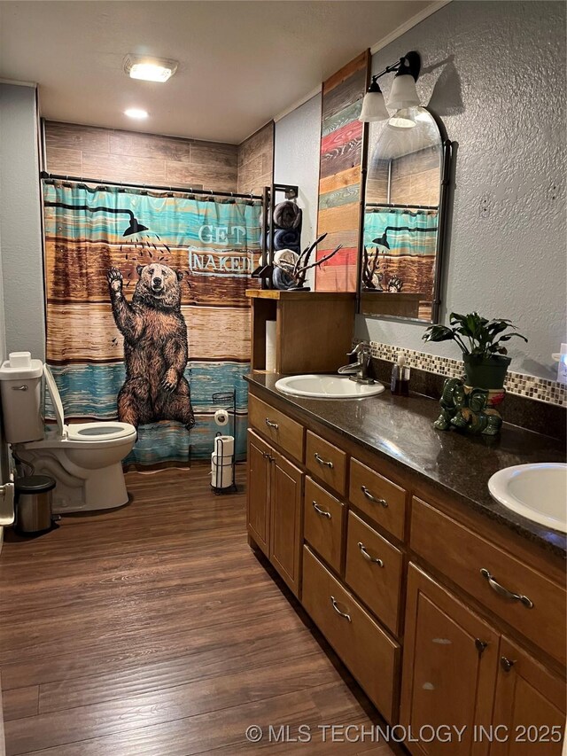bathroom with toilet, wood finished floors, a sink, and double vanity