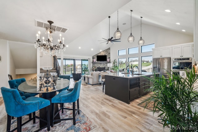 12255 Avalon Dr, Sperry, OK 74073 - dining area featuring high vaulted ceiling, ceiling fan, a fireplace, light wood-style floors, and a chandelier