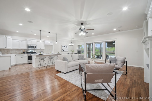 living area featuring visible vents, light wood-type flooring, recessed lighting, and ceiling fan with notable chandelier