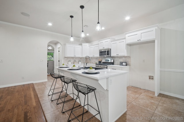 kitchen featuring arched walkways, white cabinetry, a breakfast bar, stainless steel appliances, and backsplash