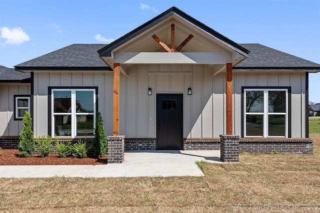 view of front of property featuring a front yard, board and batten siding, and a shingled roof