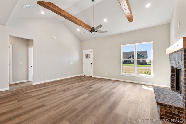 unfurnished living room featuring beamed ceiling, ceiling fan, wood finished floors, and a brick fireplace