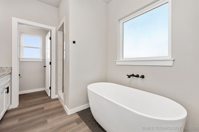 full bath with a stall shower, vanity, wood finished floors, a freestanding bath, and baseboards