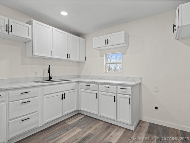 kitchen featuring baseboards, white cabinetry, a sink, and wood finished floors
