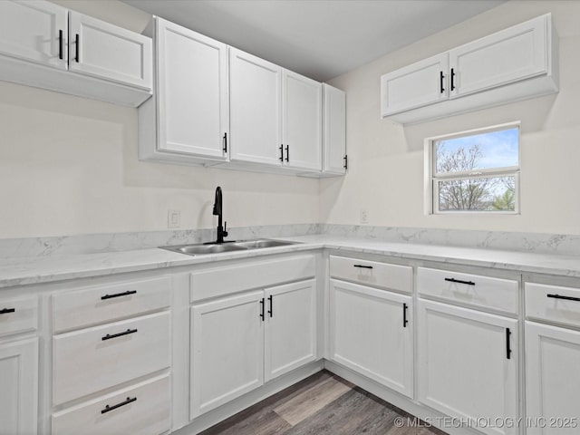 kitchen with white cabinets, a sink, light stone countertops, and wood finished floors