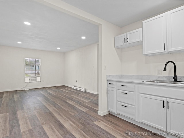 kitchen featuring baseboard heating, white cabinets, wood finished floors, and a sink