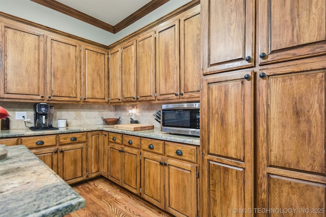 626 Countrywood Way, Sapulpa, OK 74066 - kitchen featuring stainless steel microwave, crown molding, brown cabinets, and tasteful backsplash