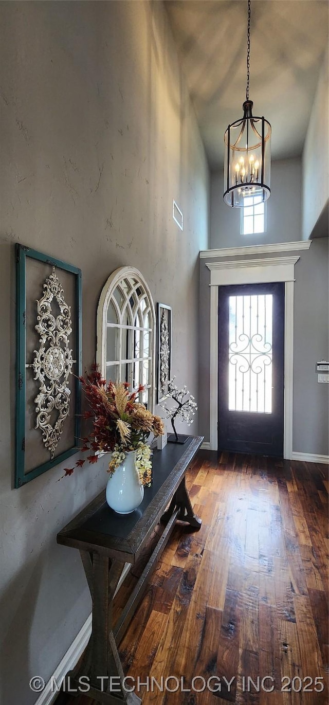 entryway featuring an inviting chandelier, wood finished floors, visible vents, and a high ceiling