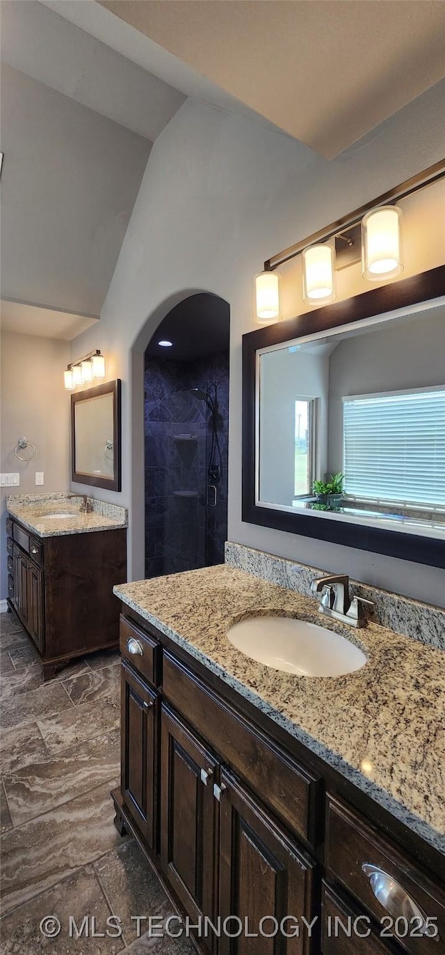 full bath with lofted ceiling, a sink, two vanities, and tiled shower