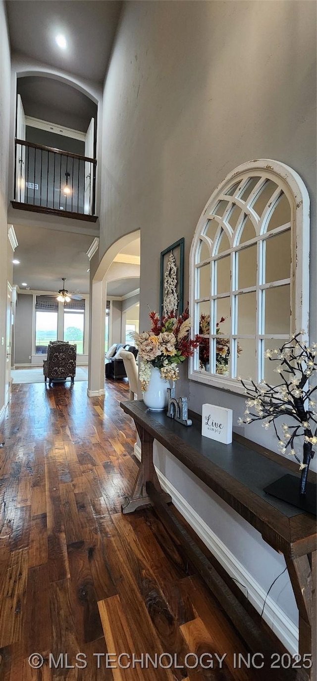 dining area featuring a high ceiling, arched walkways, wood-type flooring, baseboards, and ceiling fan