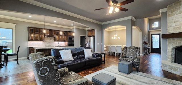living area with light wood-style flooring, arched walkways, baseboards, ceiling fan with notable chandelier, and a fireplace