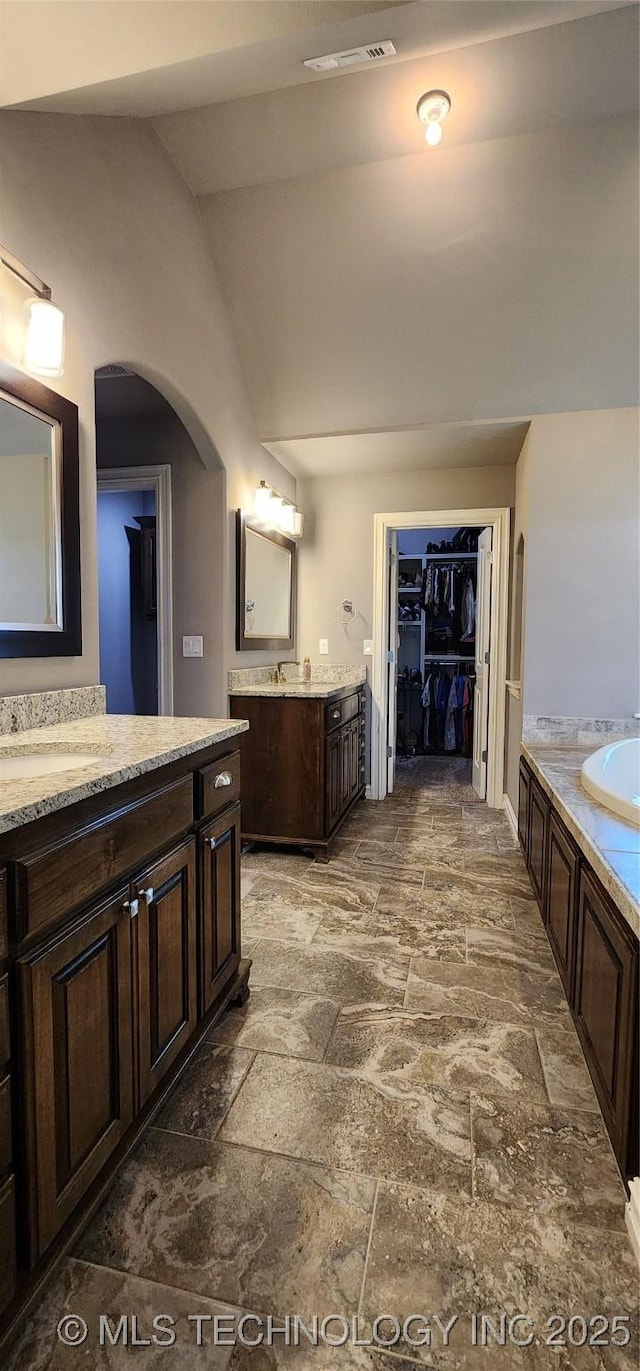 bathroom featuring lofted ceiling, stone tile floors, visible vents, a sink, and a garden tub