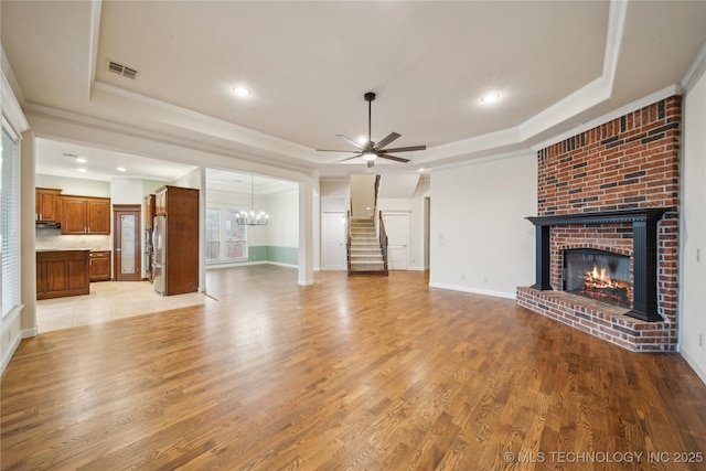 6673 E 60th Pl, Tulsa, OK 74145 - unfurnished living room featuring a tray ceiling, a brick fireplace, stairs, crown molding, and ceiling fan