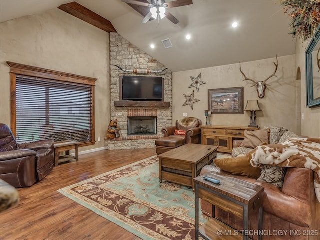 living area featuring wood finished floors, visible vents, a stone fireplace, and ceiling fan