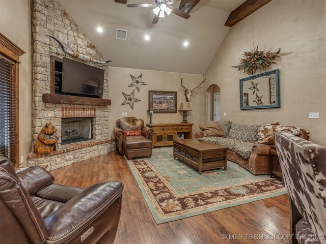 living area featuring arched walkways, visible vents, ceiling fan, hardwood / wood-style flooring, and a fireplace