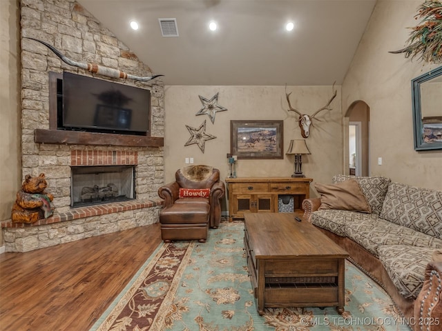 living area featuring high vaulted ceiling, wood finished floors, arched walkways, a fireplace, and visible vents