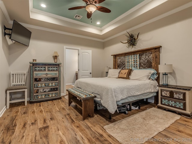 bedroom with wood finished floors, visible vents, ornamental molding, and a tray ceiling