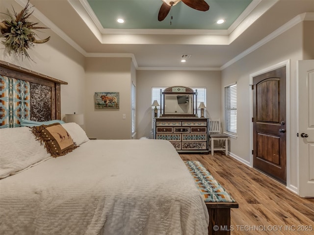 bedroom with a tray ceiling, wood finished floors, crown molding, and recessed lighting