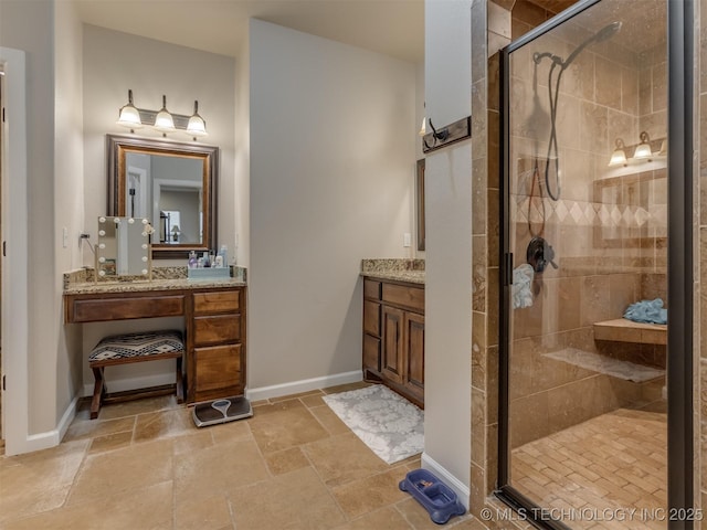 bathroom with stone tile floors, baseboards, vanity, and a shower stall