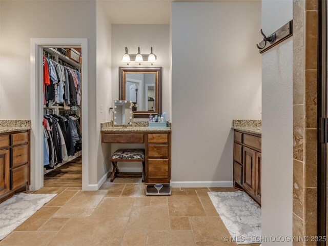 full bath featuring a walk in closet, stone tile flooring, and vanity