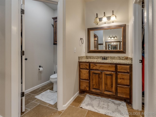 bathroom with toilet, stone finish floor, vanity, and baseboards