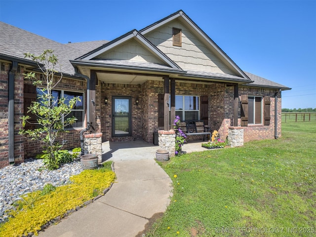 craftsman-style home featuring a porch, a front lawn, brick siding, and roof with shingles