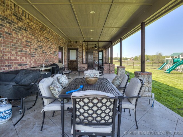 view of patio featuring a playground, fence, ceiling fan, grilling area, and outdoor dining area