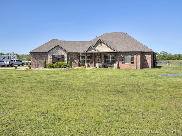 single story home featuring brick siding, a shingled roof, a front yard, and covered porch