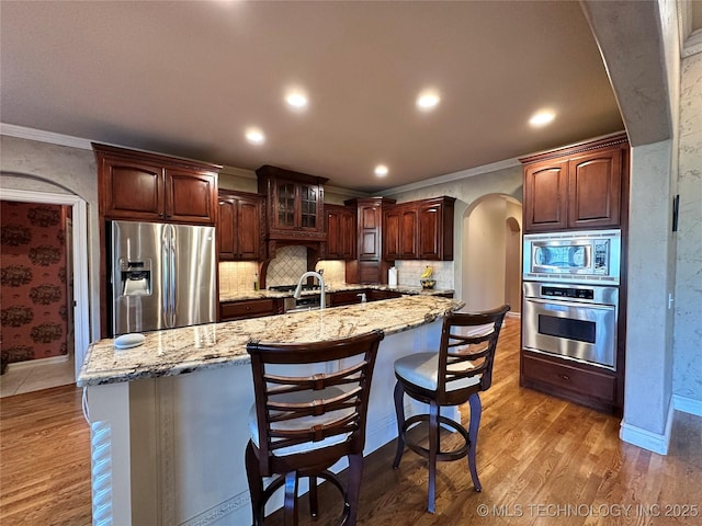 10213 S 88th E Ave, Tulsa, OK 74133 - kitchen featuring stainless steel appliances, arched walkways, ornamental molding, wood finished floors, and light stone countertops