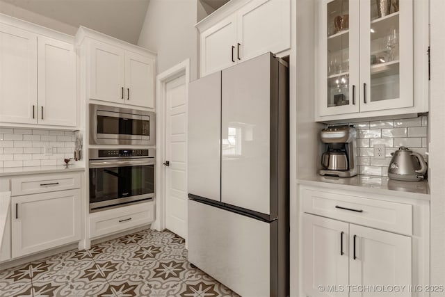 kitchen featuring glass insert cabinets, decorative backsplash, appliances with stainless steel finishes, light countertops, and white cabinetry