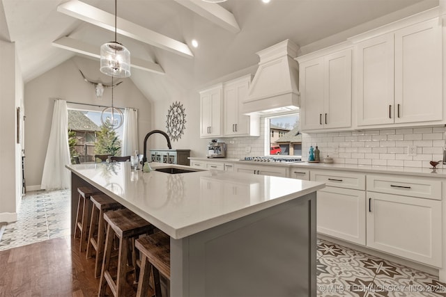 kitchen with premium range hood, a healthy amount of sunlight, a center island with sink, and a sink