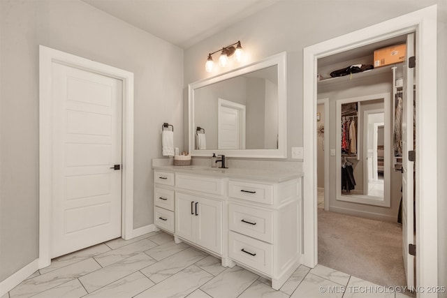 bathroom with marble finish floor, a walk in closet, vanity, and baseboards