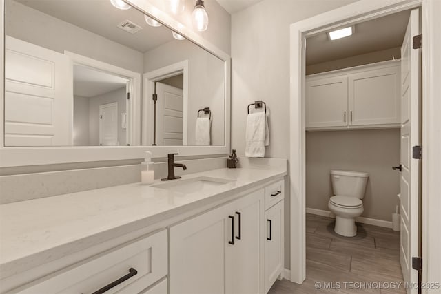 bathroom featuring visible vents, baseboards, toilet, wood finished floors, and vanity