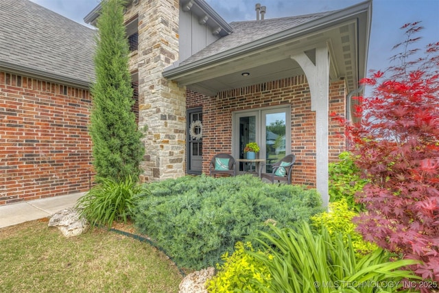 entrance to property featuring a shingled roof and brick siding