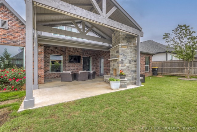 rear view of house with a patio area, an outdoor living space with a fireplace, a lawn, brick siding, and fence