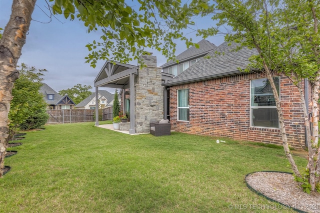 back of house with a yard, brick siding, fence, a shingled roof, and a patio area